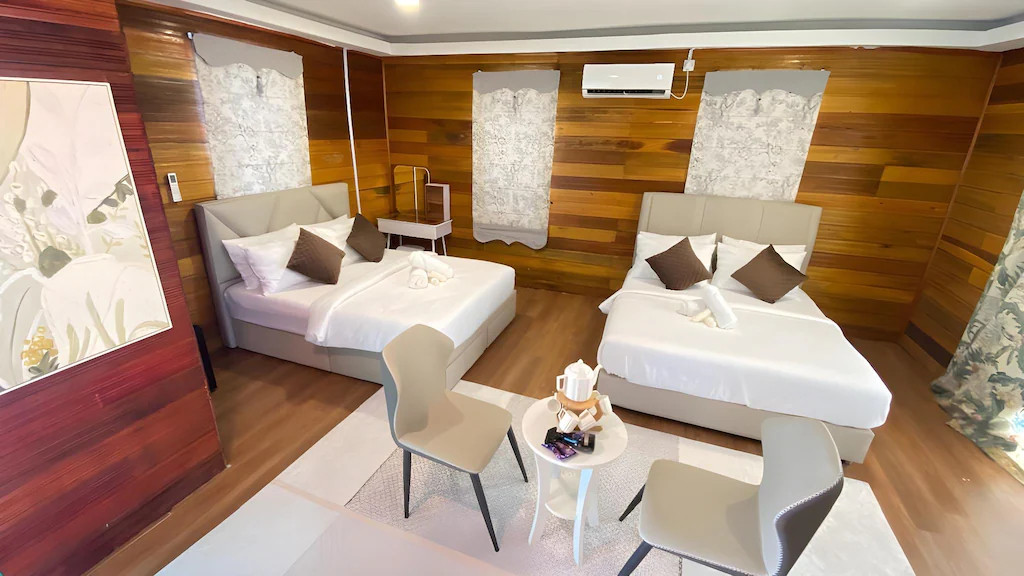 A bright bedroom at Blue Ocean Resort in Semporna offering two large beds, modern style orange chairs, elegant wood floors, and AC.