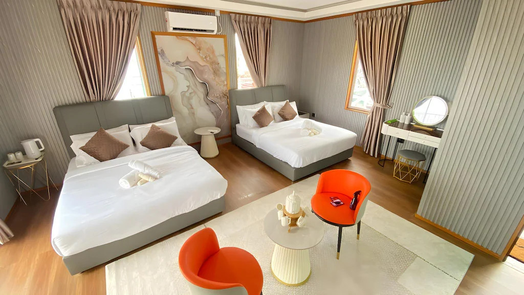 A colorful bedroom at Blue Ocean Resort near Tun Sakaran Marine Park offering two large beds, modern style orange lounge chairs, large abstract wall art, sleek wood floors, and an AC unit.