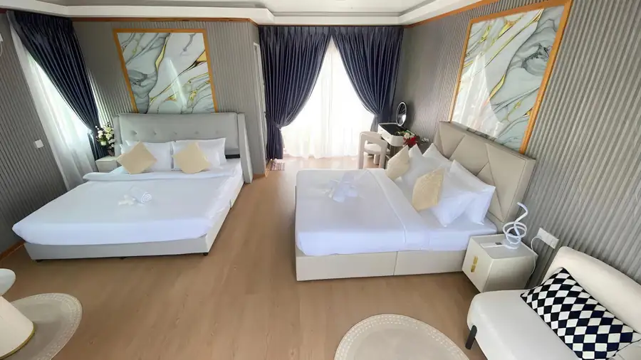 A bright family bedroom at Blue Ocean Resort over the Celebes Sea featuring two large beds, modern style orange chairs, a vanity desk, elegant hardwood floors, and air con.