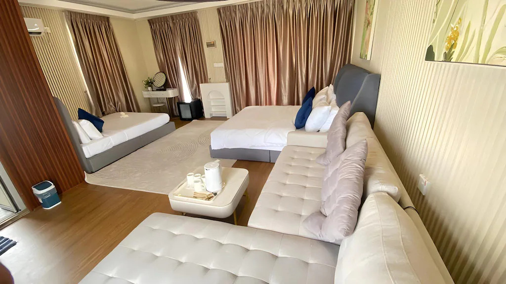 A large family bedroom featuring two double beds with towel art, elegant grey wall paneling, a vanity desk, and a seating area, presenting an upscale local style at Blue Ocean Resort.