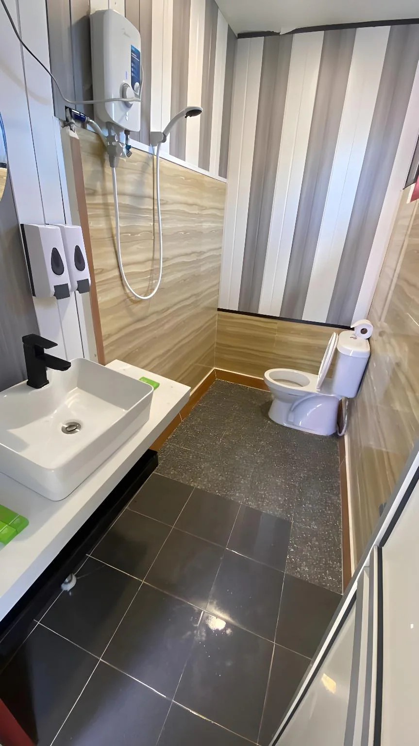 A well-appointed bathroom at Blue Ocean Resort highlighting a compact modern washbasin, a vanity mirror, a clean toilet, and a corner glass shower stall fitted with an electric shower system.
