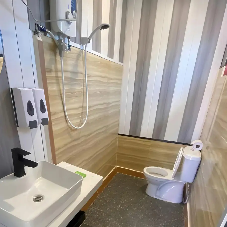 A well-appointed bathroom at Blue Ocean Resort highlighting a compact modern washbasin, a vanity mirror, a clean toilet, and a corner glass shower stall fitted with an electric shower system.