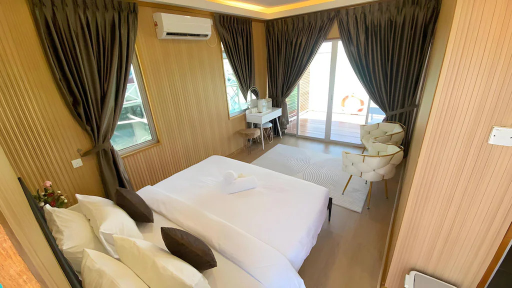 A comfortable bedroom at Blue Ocean Resort in the Semporna archipelago featuring one large bed with a modern metal frame, traditional style wooden walls with polished wood floors, and AC.