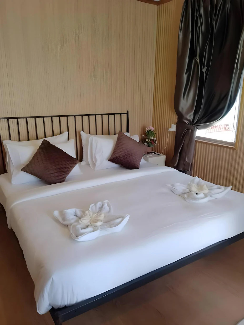 A traditional style bedroom at Blue Ocean Resort near Bum Bum Island offering a large bed, swan towel art, brown accent pillows, wood paneling, warm wooden plank floors, and A/C.